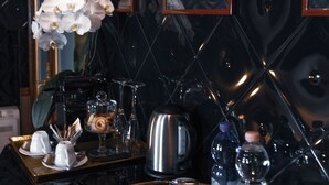 A dining area with a tray of white teacups and saucers, a vase of white orchids, and framed posters on the wall. - Ilsanleonardo - Suites (Bergamo)