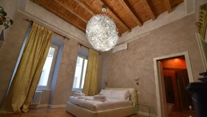 A bedroom with a wooden ceiling, a large chandelier, a bed with towels, and a view of a bathroom. - Ilsanleonardo - Suites (Bergamo)