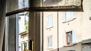A window with a brass handle, a view of a street with parked cars and a building with balconies and shutters. - Ilsanleonardo - Suites (Bergamo)