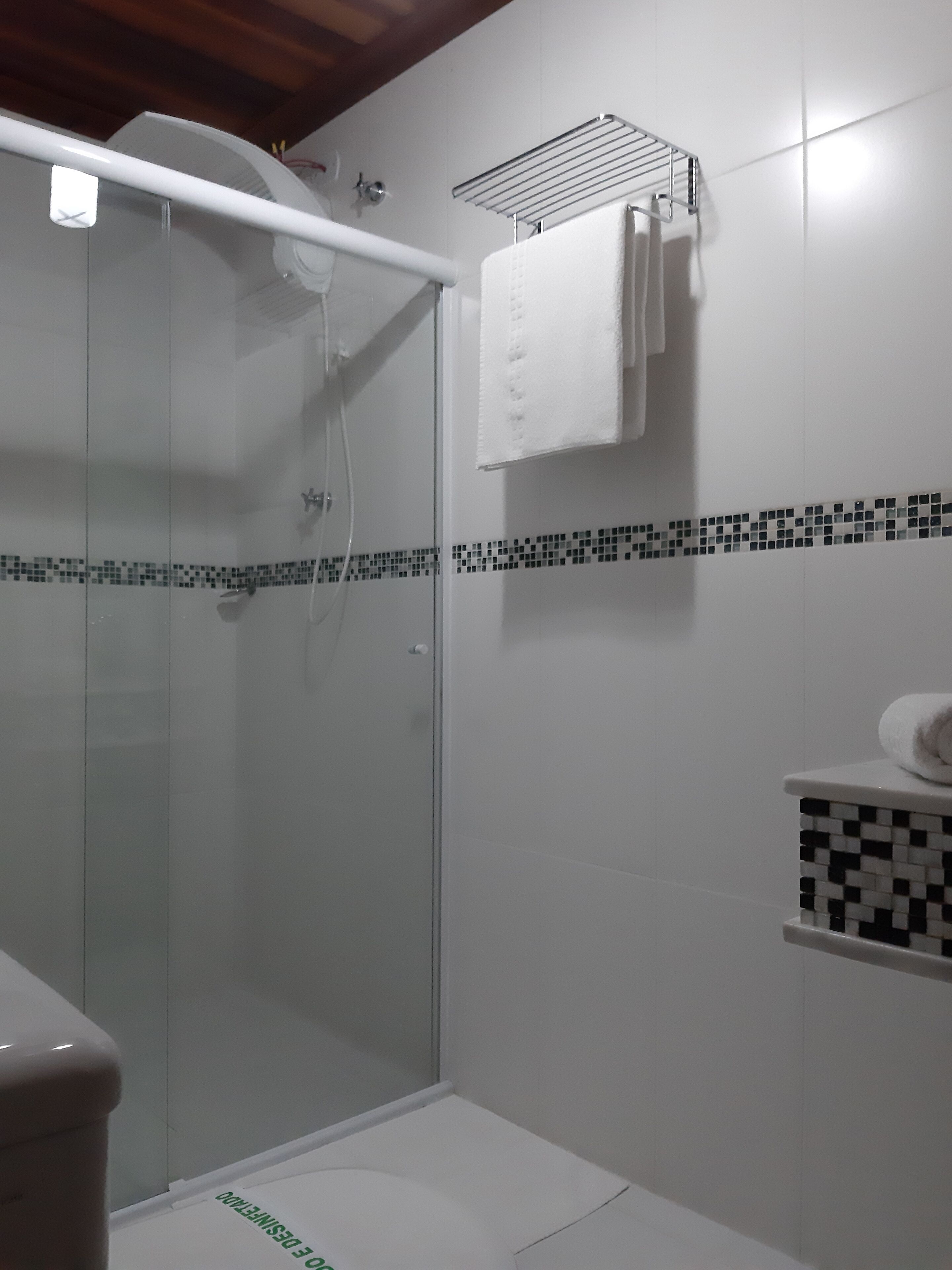 Ein Duschbereich mit Glastür, ein weißes Handtuch auf einem Haken und eine geflieste Wand mit Schwarz-Weiß-Muster.