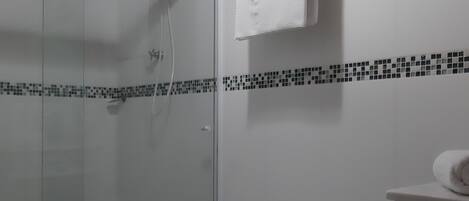 Ein Duschbereich mit Glastür, ein weißes Handtuch auf einem Haken und eine geflieste Wand mit Schwarz-Weiß-Muster.
