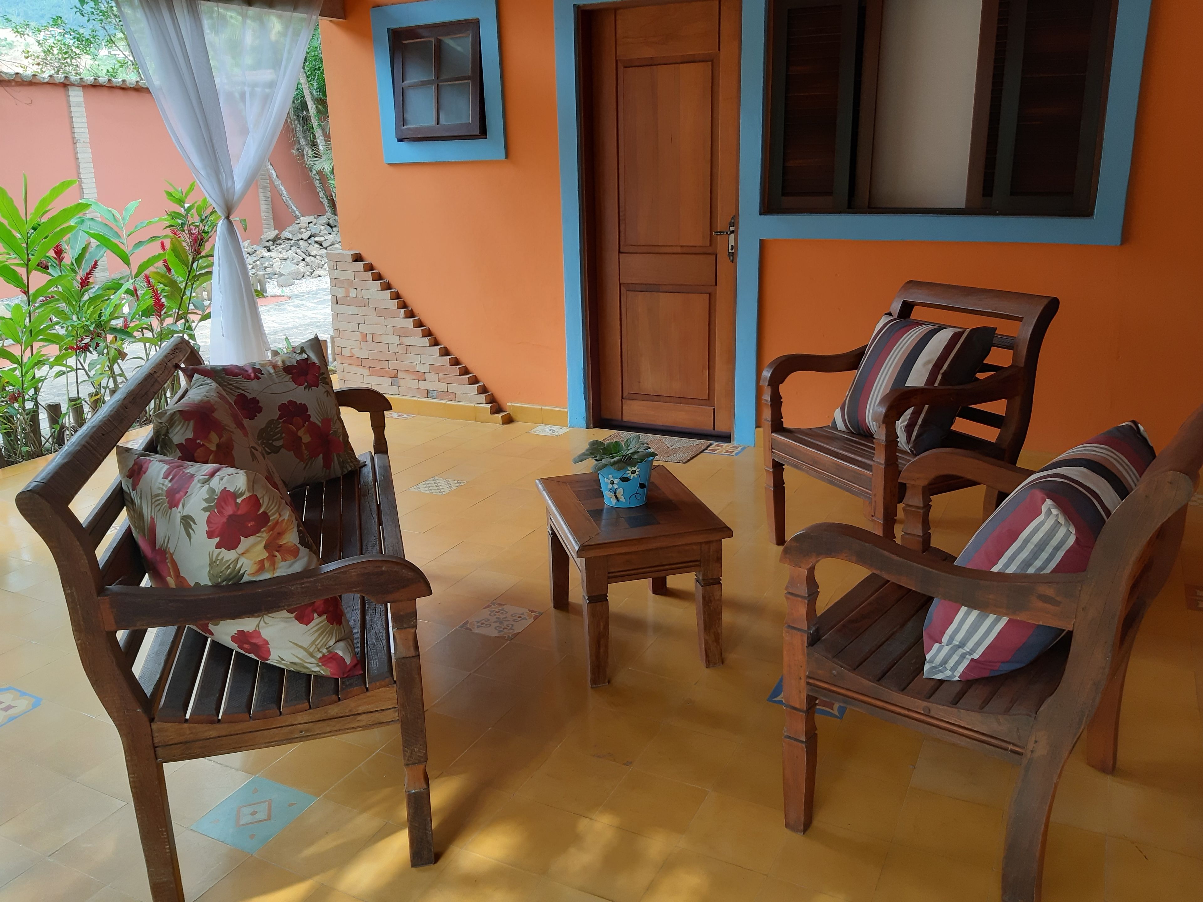 Un espace extérieur accueillant, aménagé avec du mobilier en bois et une petite table, un escalier en briques et une porte dotée d’une fenêtre.