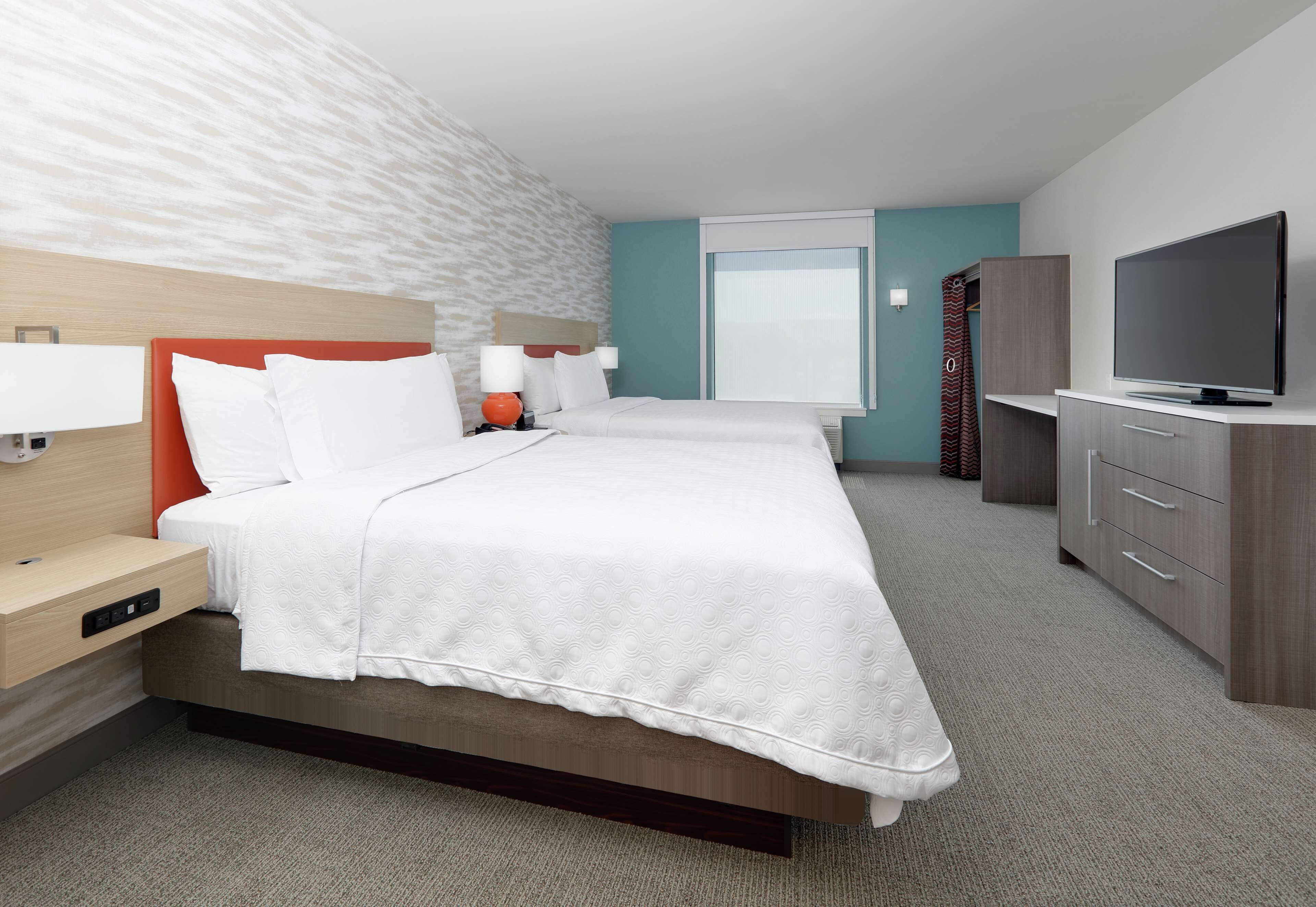 A hotel room with a large bed, a TV, a desk with a lamp, and a wardrobe.