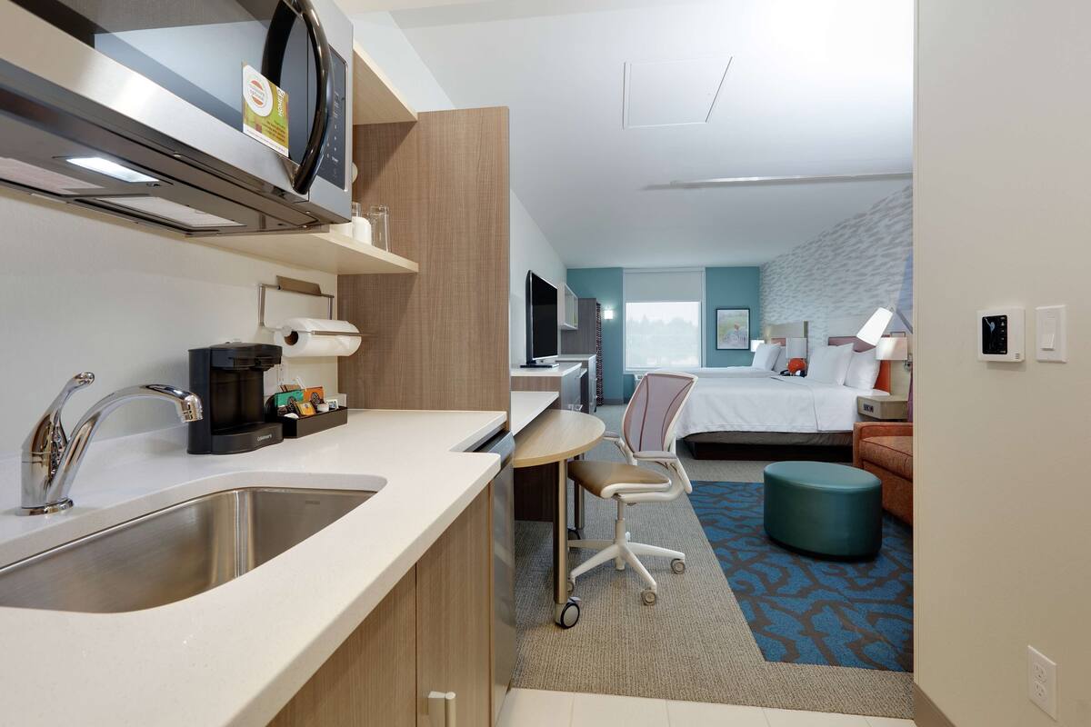 Une chambre d’hôtel moderne équipée d’une kitchenette, d’un lit, d’un bureau et d’un coin salon.