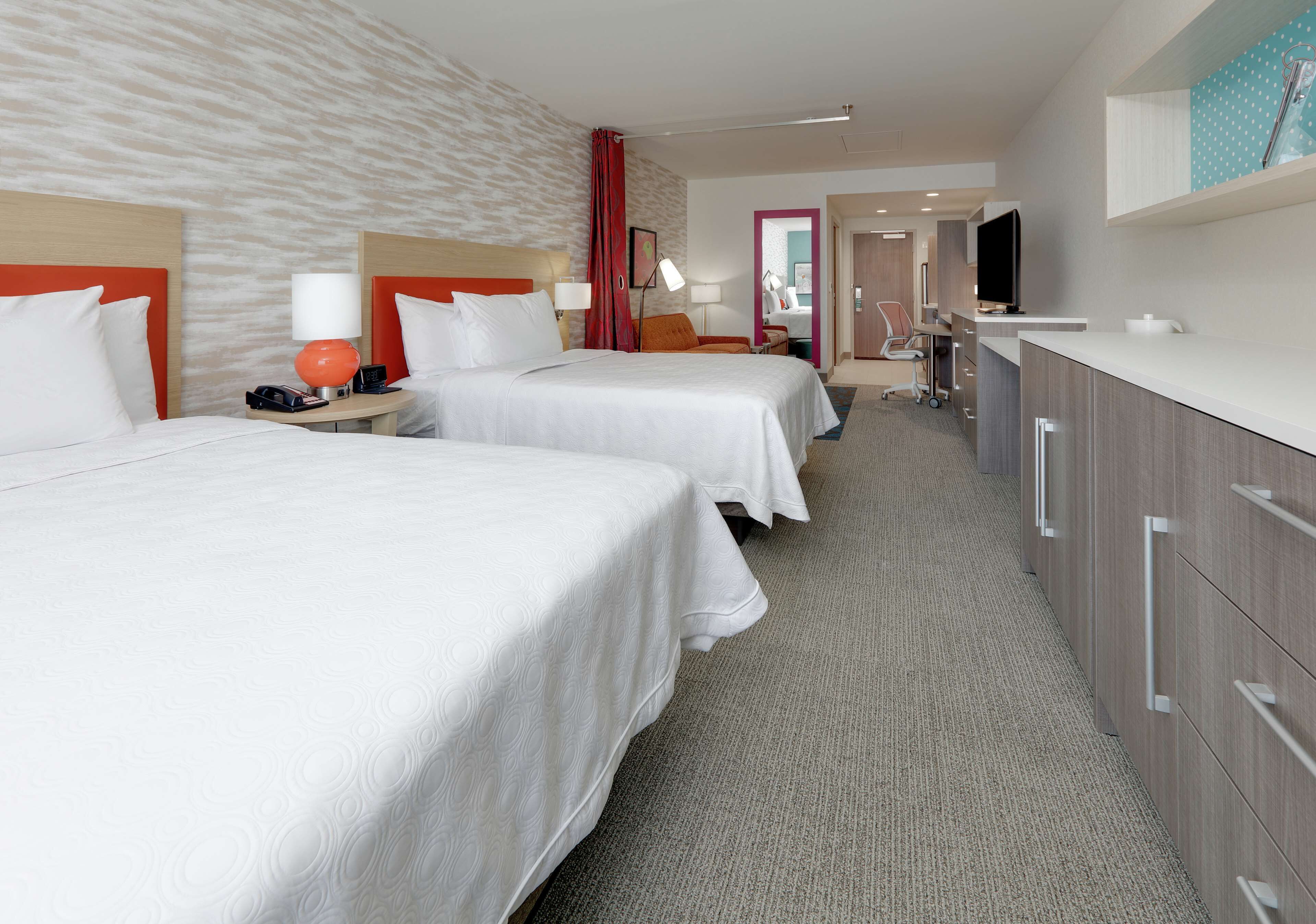 A hotel room with two beds, a desk, a TV, and a minibar.