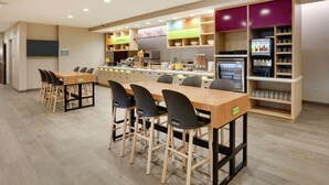 A modern kitchen area with multiple bar stools, a refrigerator, and a coffee machine.