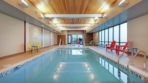 An indoor swimming pool with clear blue water, wooden ceiling, and bright lighting.
