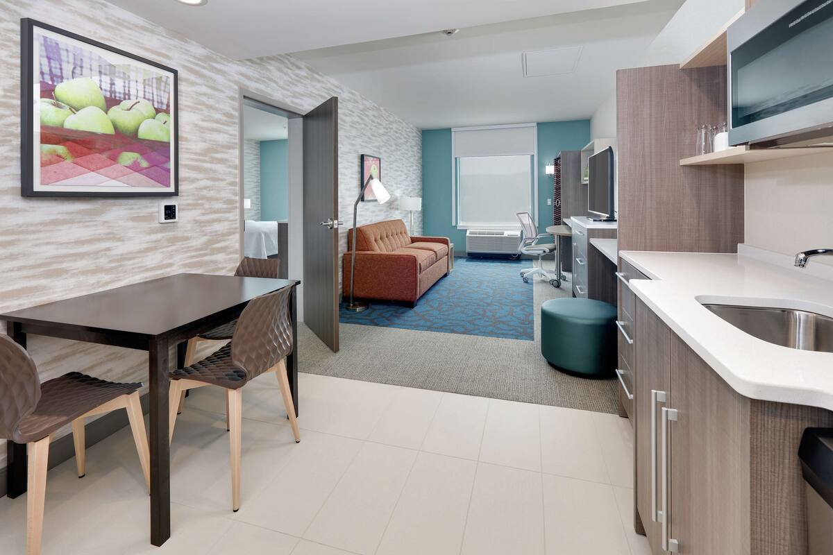Une chambre d’hôtel moderne dotée d’un coin repas, d’une kitchenette et d’un espace de vie avec un canapé et une télévision.