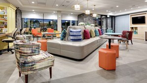 A modern hotel lobby with a seating area, a reception desk, and a large window offering a view of the outdoors.