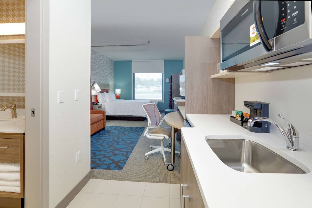 Une chambre d’hôtel moderne dotée d’une kitchenette, d’un lit avec vue, d’un bureau et d’une salle de bain avec douche et lavabo.
