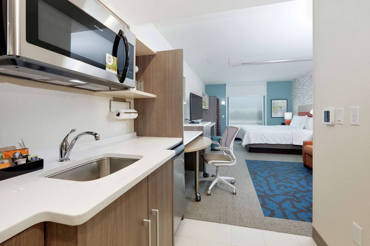 Une chambre d’hôtel moderne équipée d’une kitchenette, d’un lit, d’un bureau et d’une salle de bain.
