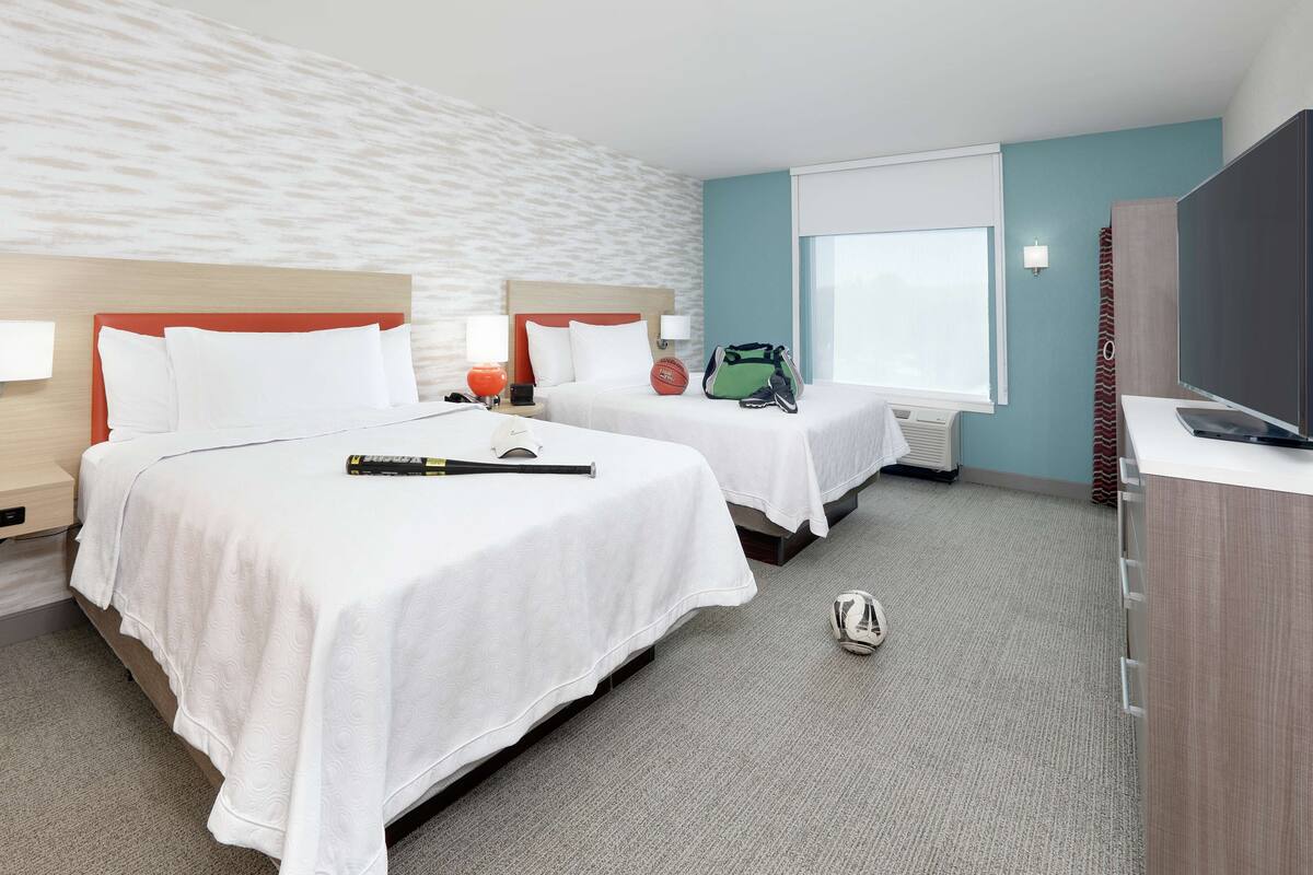 Une chambre d’hôtel avec deux lits, une télévision, un bureau et une fenêtre.