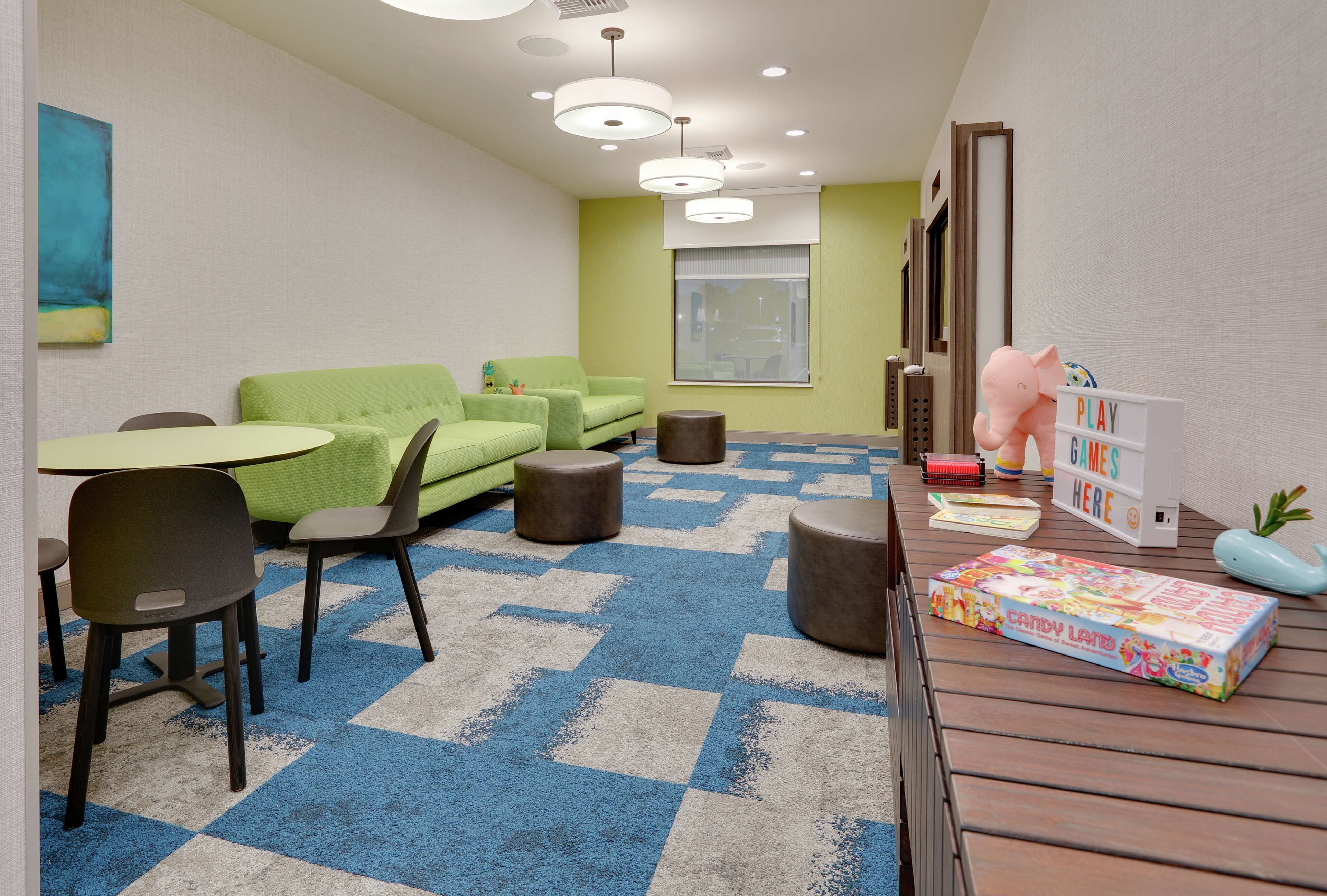 A modern room with a green sofa, a round table, and a play area with a sign that says "PLAY GAMES HERE".