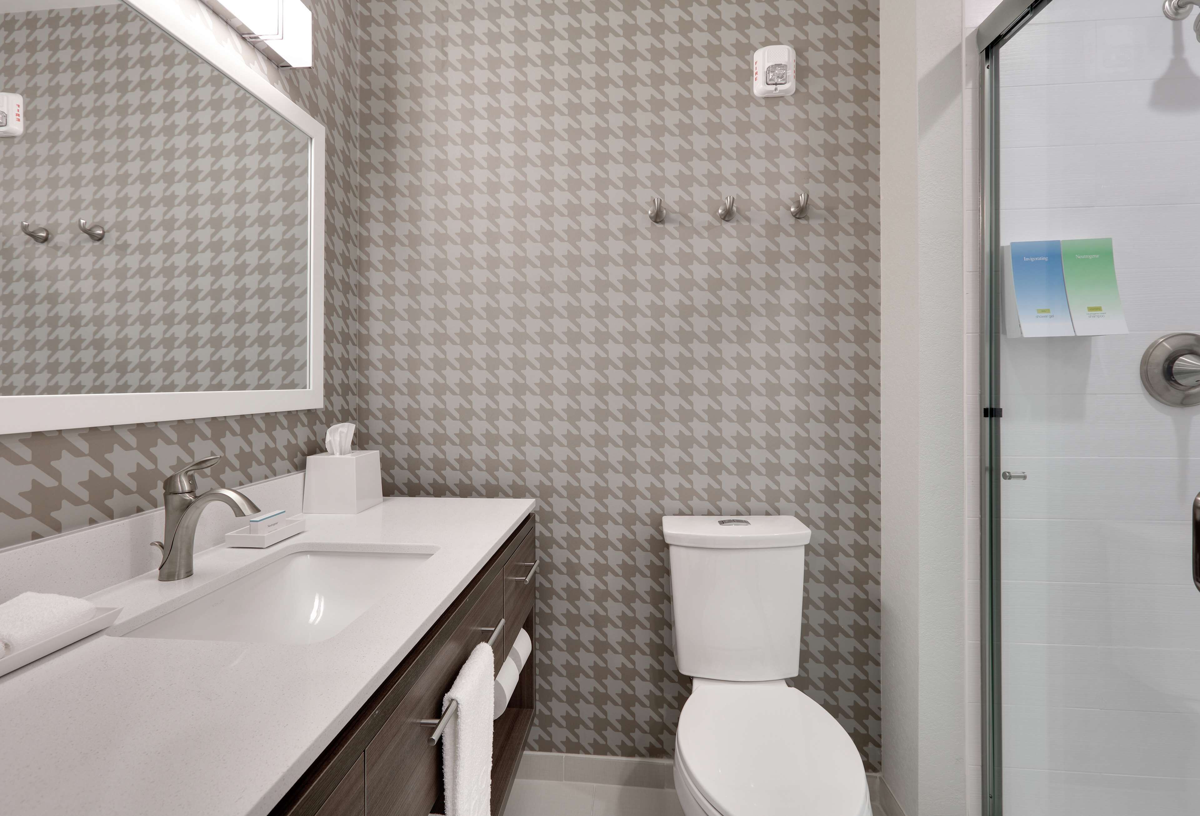 A bathroom with a houndstooth patterned wall, a white sink with a modern faucet, a toilet, and a glass shower enclosure.