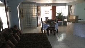 A living room with a sofa, dining table, chairs, and a kitchen area with a counter and cabinets. - Villa Edinburgh (Montego Bay)