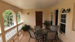 A covered patio with a round table and chairs, potted plants, and decorative ironwork windows. - Villa Edinburgh (Montego Bay)