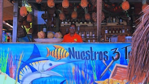 A colorful mural with fish and a boat, a counter with a bowl of coconuts, and hanging pineapples.