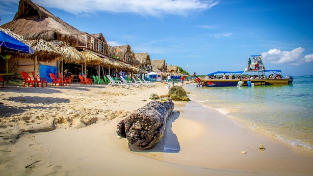 A beach with thatched-roof buildings, a sandy shore, and a boat in the water.