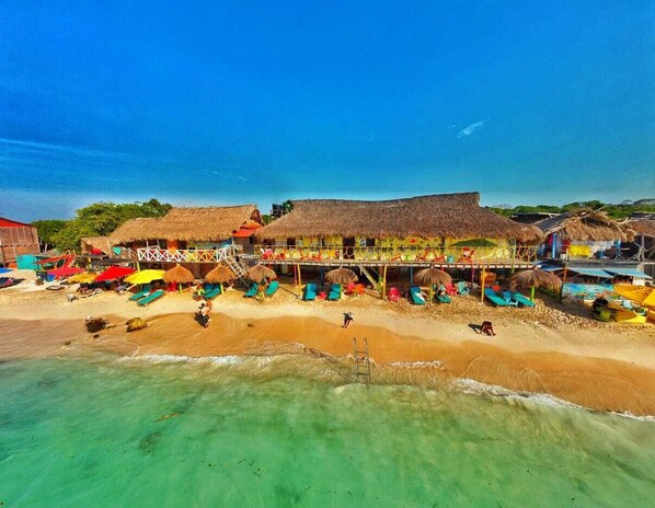 Resort à beira-mar com estruturas de palha, guarda-sóis coloridos e cadeiras de praia.