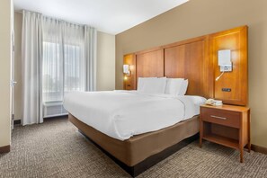 A hotel room with a large bed, a bedside table with a phone, and a wall-mounted light fixture. - Comfort Suites Greensboro - High Point (Greensboro)