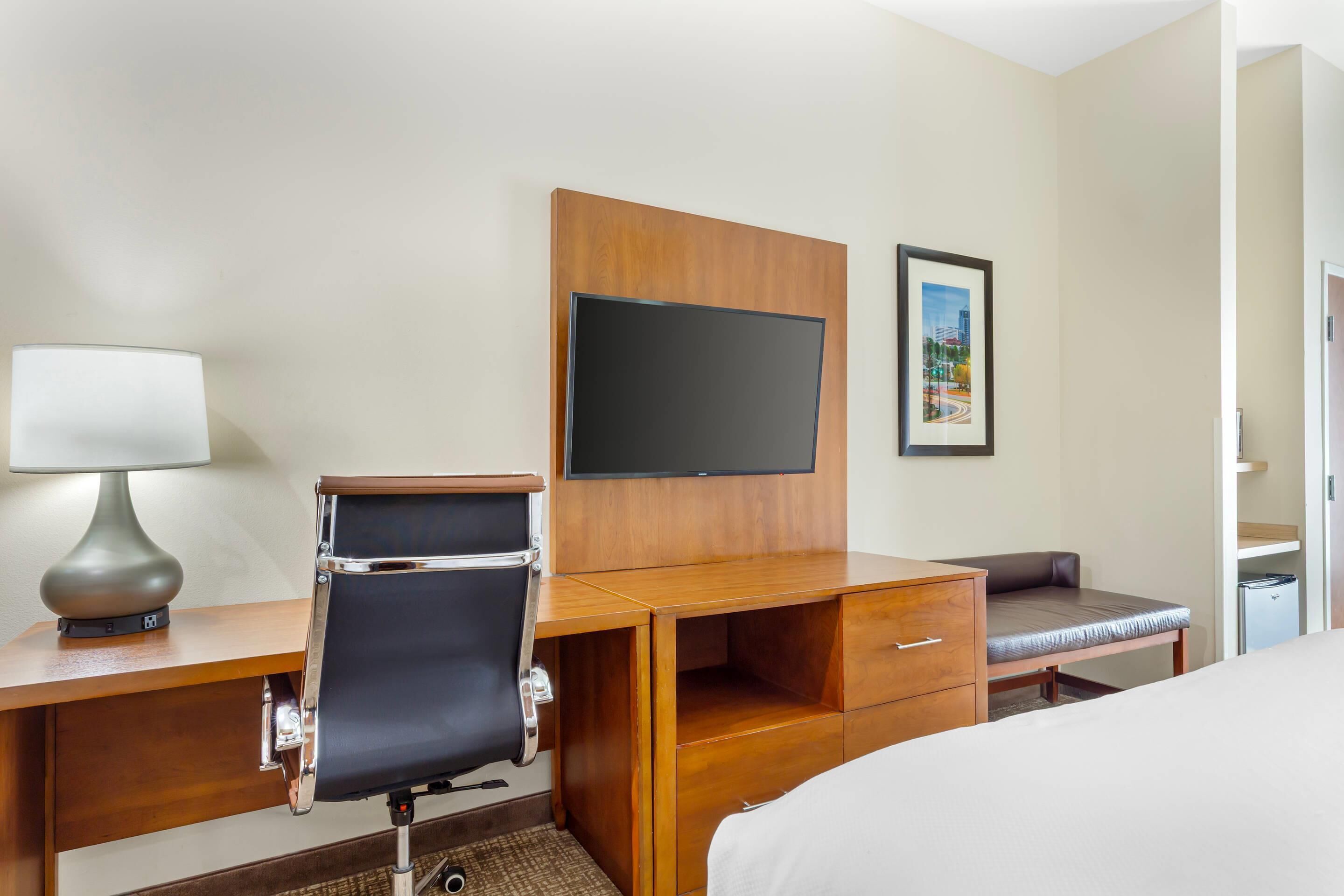 Une chambre d’hôtel avec un bureau en bois, une chaise, un lit, une télévision et un tableau encadré au mur.