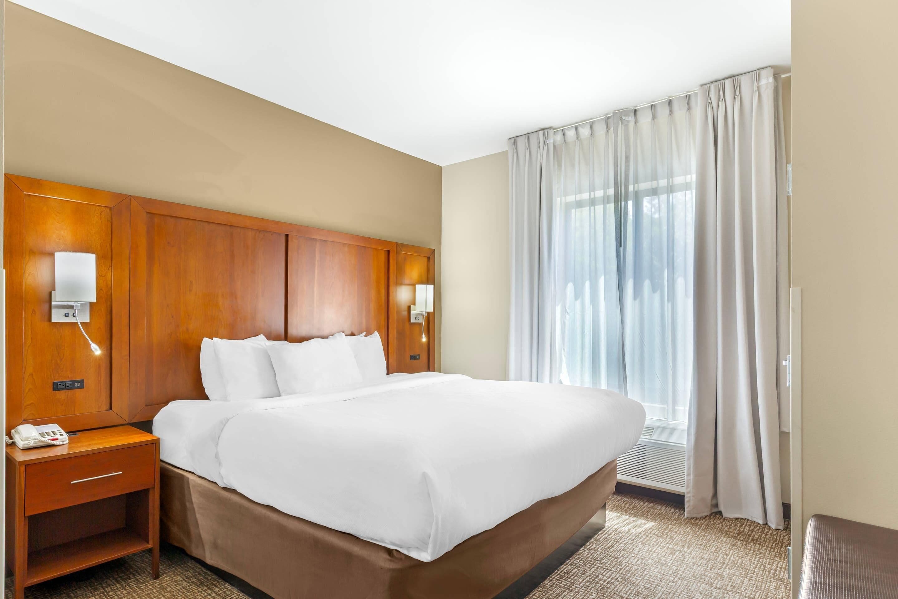 A hotel room with a large bed, wooden headboard, bedside lamps, a telephone, and a window with curtains.