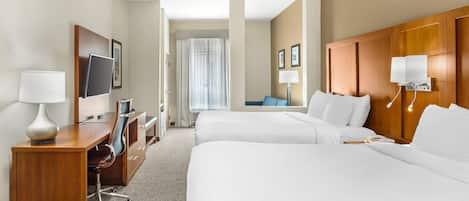 A hotel room with two beds, a desk with a chair, a TV, and a bathroom visible through a door.