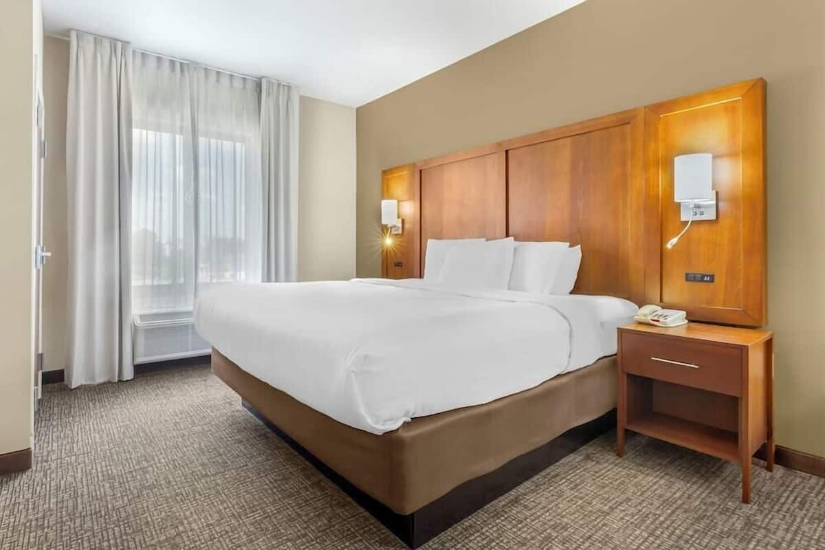 A hotel room with a large bed, a wooden headboard, bedside lamps, a telephone, and a window with curtains.
