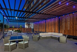 Een terras buiten met een houten pergola, rieten meubels en een zithoek.