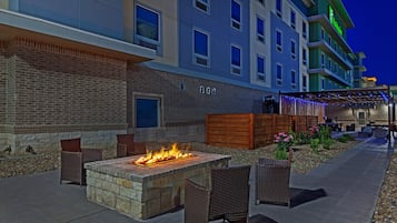 A hotel with a brick facade, outdoor seating area with chairs and a fire feature, and a covered walkway with string lights.