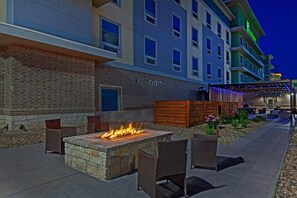 A hotel with a brick facade, outdoor seating area with chairs and a fire feature, and a covered walkway with string lights. - Holiday Inn Amarillo East (Amarillo)