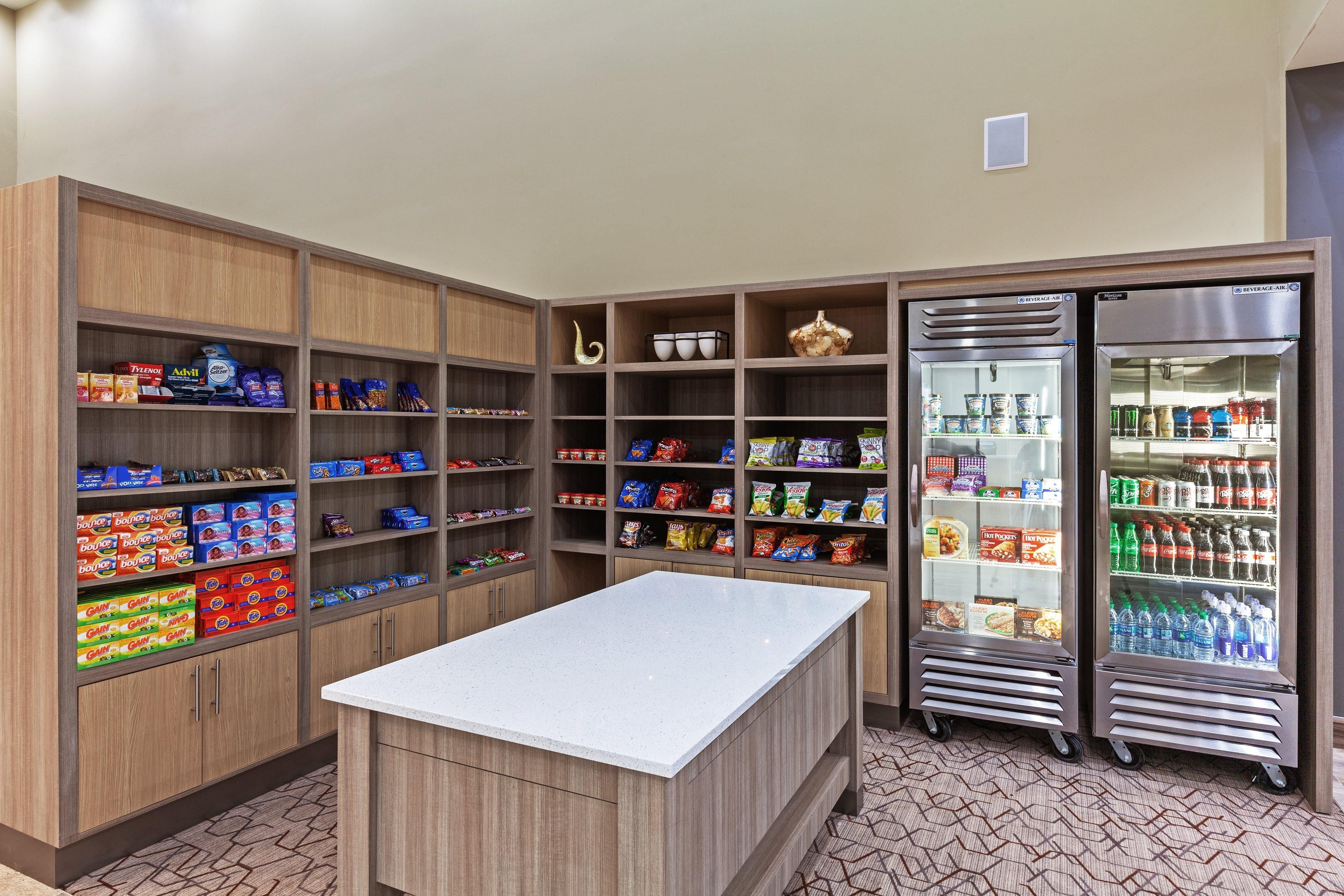 A kitchenette with wooden cabinets, a white countertop, and two refrigerators stocked with beverages and snacks.
