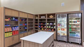 A kitchenette with wooden cabinets, a white countertop, and two refrigerators stocked with beverages and snacks.