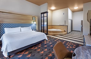 Een hotelkamer met een bed, een badkamer met een badkuip, en een klein tafeltje met een stoel.