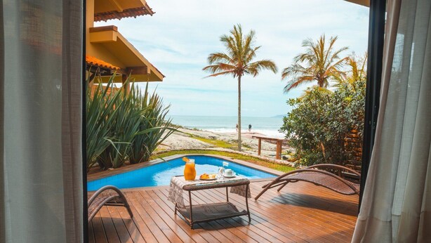 Une terrasse en bois avec une piscine, du mobilier d’extérieur et une vue sur la plage et l’océan.