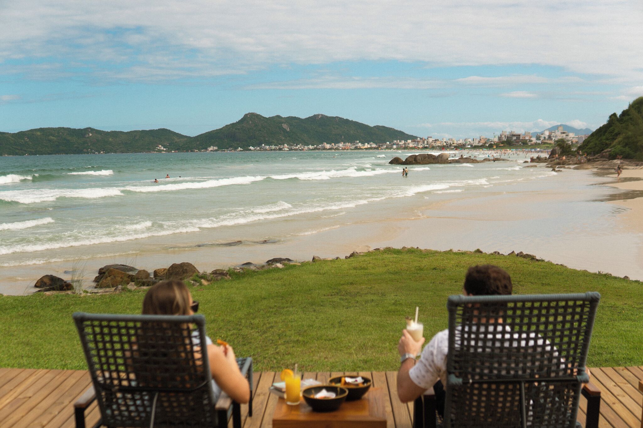 A beachside dining area with a view of the ocean and distant hills.