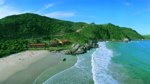 Une plage avec un complexe hôtelier, des eaux turquoise cristallines et des collines verdoyantes.