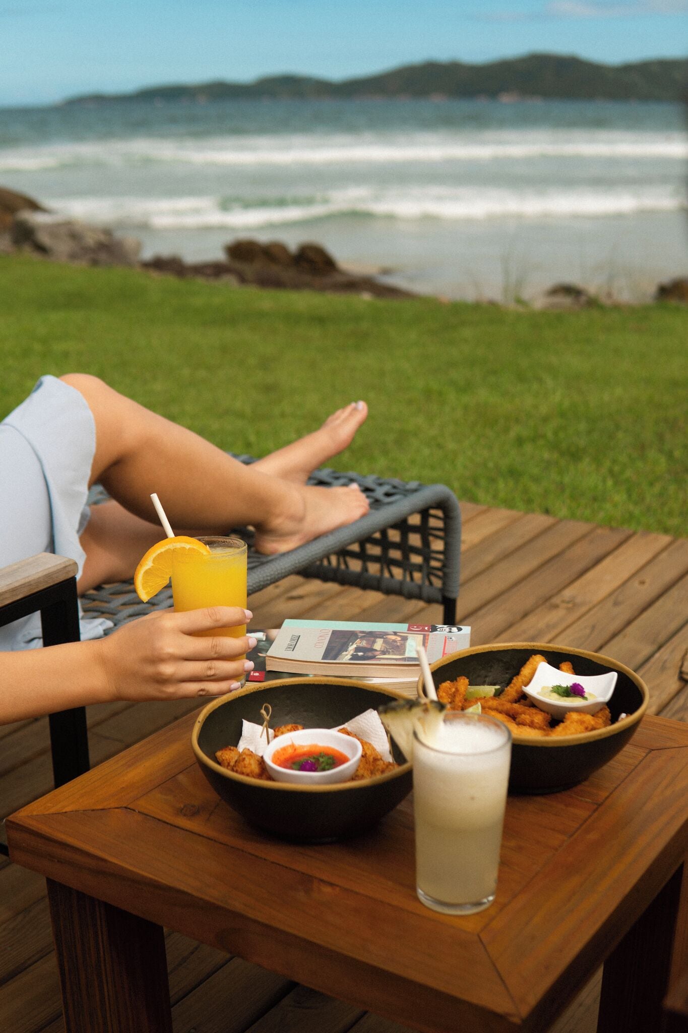 A person relaxing on a deck with a table set for a meal, overlooking a body of water.