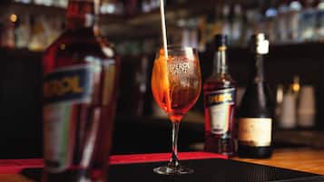 A bar setting with a glass of Aperol Spritz, a bottle of Aperol, and a bottle of wine on a bar mat.