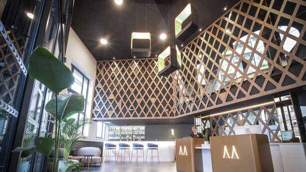 Un espace d’accueil moderne doté d’une cloison en bois aux motifs géométriques, d’un comptoir d’accueil et d’un bar.