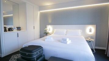 A hotel room with a large bed, a bedside table, a nightstand, a mirror, a wardrobe, and a suitcase.
