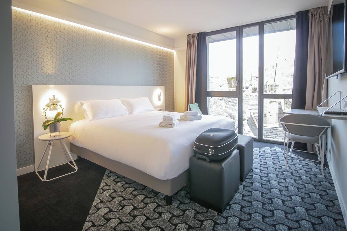 A modern hotel room with a large bed, a desk, and a view of the city.