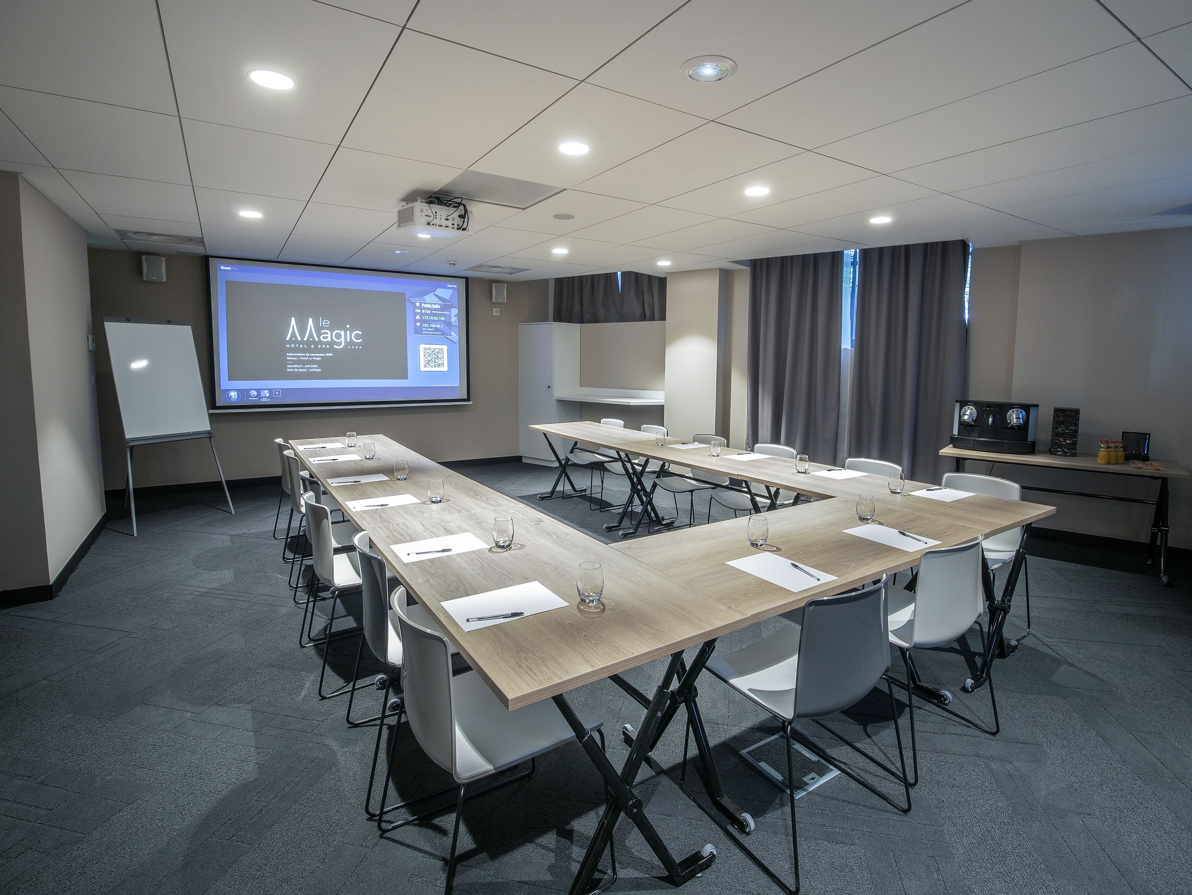 A conference room with a long table, chairs, a whiteboard, and a projector screen displaying a presentation.