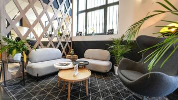 Un espace de détente moderne avec un sol à motifs géométriques, deux canapés, une table ronde en bois et des plantes en pot.