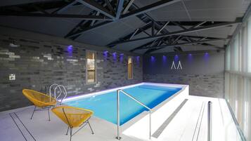 Une piscine intérieure moderne avec un sol carrelé, deux chaises jaunes et un plafond avec des poutres apparentes.