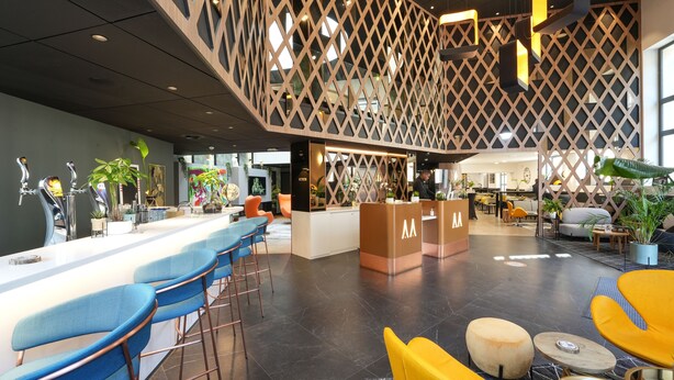A modern bar area with a counter, bar stools, and a seating area with yellow chairs. - Hôtel Le Magic & Spa (Vitre)