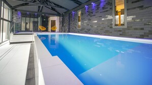 Une piscine intérieure à l’eau d’un bleu limpide, avec des murs carrelés et un éclairage moderne.