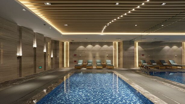 Una piscina interior moderna con suelo de baldosas azules, sillones de descanso e iluminación empotrada.