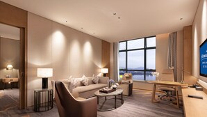 Habitación de hotel moderna con sofá, sillón, escritorio y un amplio ventanal con vistas a la ciudad.