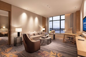 Une chambre d’hôtel moderne équipée d’un canapé, d’un fauteuil, d’un bureau et d’une grande fenêtre donnant sur la ville.